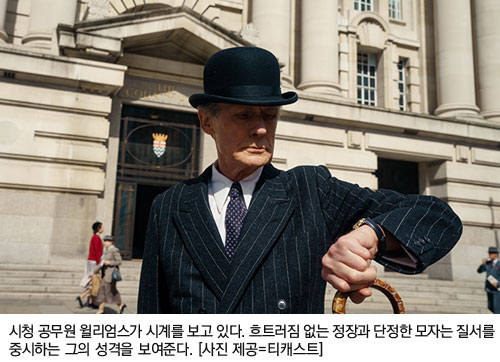 시청 공무원 윌리엄스가 시계를 보고 있다. 흐트러짐 없는 정장과 단정한 모자는 질서를 중시하는 그의 성격을 보여준다. [사진 제공=티캐스트]